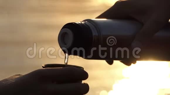 斯洛莫日落时分人们用手把水瓶里的水倒进河岸上的杯子里视频的预览图
