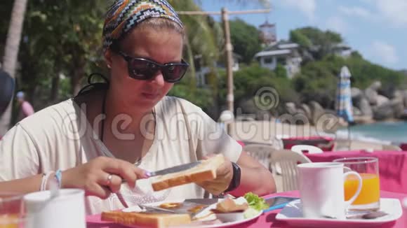 戴着头巾和太阳镜的女人在海边的海滩餐厅用黄油涂面包美味的美国视频的预览图