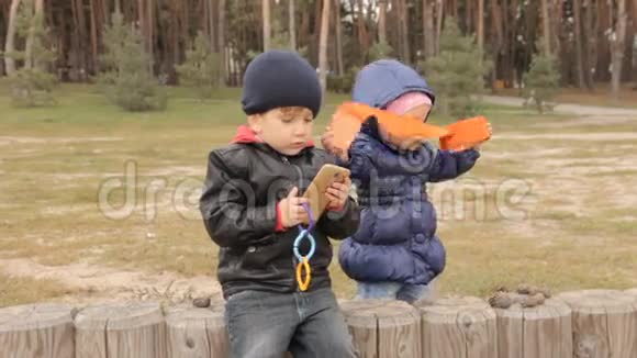 一个小女孩往旁边看一个三岁的男孩在她旁边坐在孩子的手机上按按钮视频的预览图