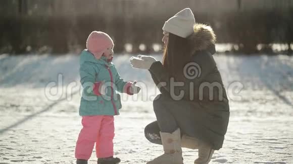 可爱的小女孩看着她的母亲那是把雪从手中吹走冬行期间快乐家庭视频的预览图