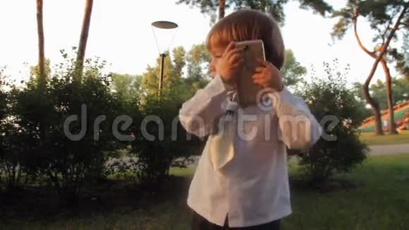 一个小男孩接电话在智能手机上交谈夏天日落视频的预览图