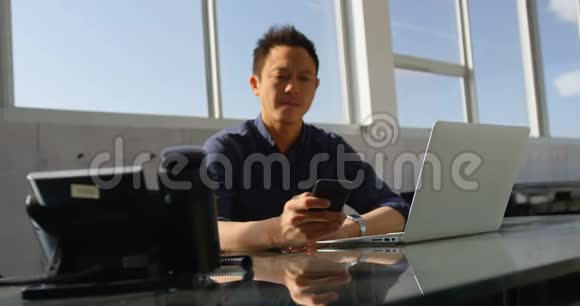 亚洲商界男性高管在办公室办公桌上使用手机视频的预览图
