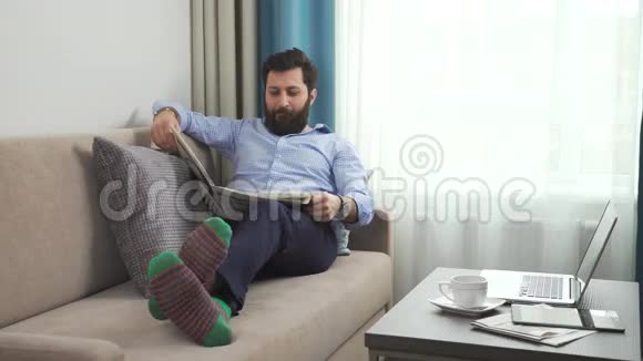 一个穿着便装的男人一双带报纸的沙发上穿着滑稽的亮袜子视频的预览图
