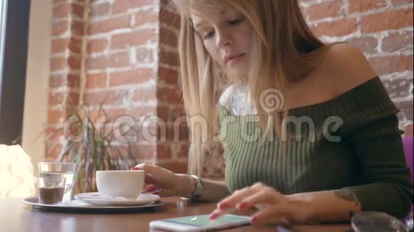 年轻漂亮的女人在咖啡馆里喝咖啡用智能手机视频的预览图