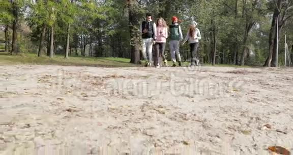 年轻人集体散步使用智能手机两对情侣牵手户外早秋公园视频的预览图