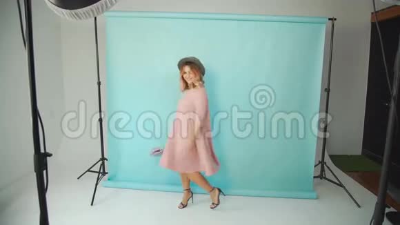 一个穿着粉红色连衣裙戴着帽子带着手提包的女人在摄影棚里拍照视频的预览图