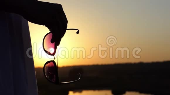 一个年轻苗条的女人站在斯隆莫的夕阳下手里拿着太阳镜视频的预览图
