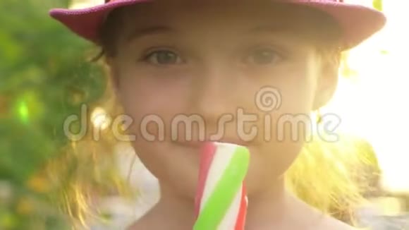 戴帽子的孩子舔冰淇淋女孩正在吃美味的奶油冰淇淋用草莓棒涂成五颜六色的冰淇淋视频的预览图
