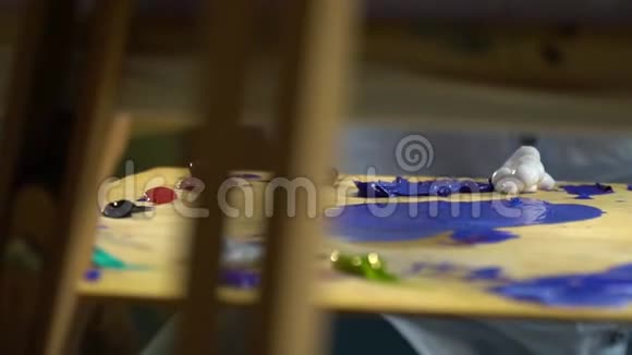 女性的手与画笔混合在木制调色板上涂上不同颜色的油画从画布后面观看视频的预览图