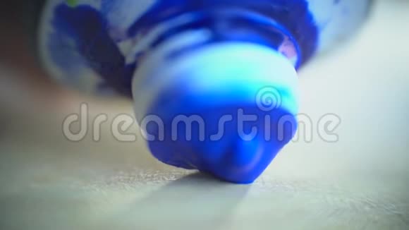 一滴蓝色的颜料从蓝色的管子里流出到木制的调色板上宏观地拍摄视频的预览图
