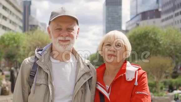 幸福的老夫妇站在街上的肖像看着摄像机背景上的城市景观视频的预览图