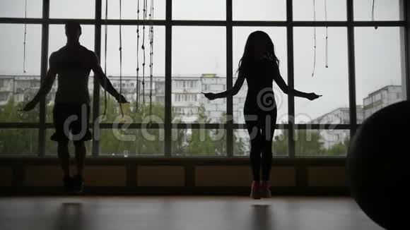 健身馆里的健身运动的女人和肌肉靠近窗户的绳子上剪影视频的预览图