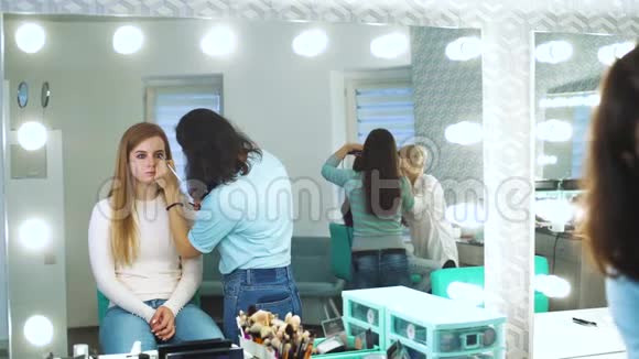 女化妆师在美容院对年轻女子施化妆品的镜像视频的预览图