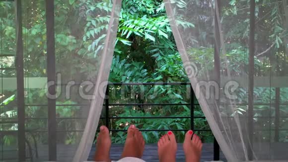 浪漫的情侣睡在床上白色的窗帘和双脚朝窗外敞开着茂密的热带绿色植物视频的预览图