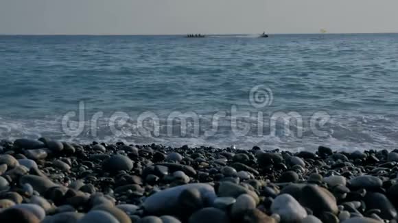 人们坐在海上的充气香蕉上带有泡沫的大透明波海卵石滩五颜六色的石头视频的预览图