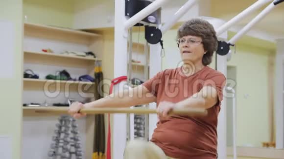 老年妇女伸展身体在健身室用棍子做理疗健康体操积极主动视频的预览图