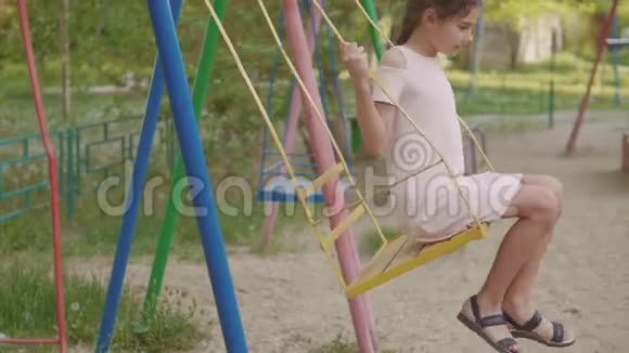小女孩在一个旧的秋千慢动作视频上摇摆在街上玩耍的女学生在荡秋千的童年视频的预览图