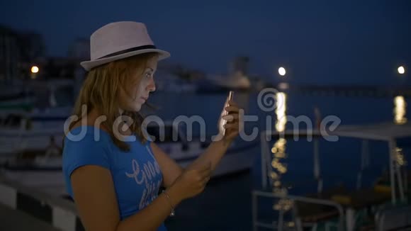 美丽快乐的女孩用智能手机拍下美丽的夜晚城市视频的预览图
