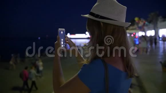 美丽快乐的女孩用智能手机拍下美丽的夜晚城市视频的预览图