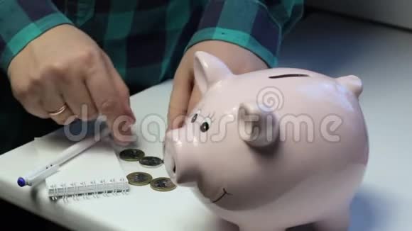 桌子上有一只粉红色的猪形的储蓄罐那个人从硬币桌上把它们扔进了储蓄罐做了很多视频的预览图