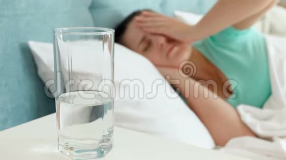 4k片头痛的年轻女子躺在床上喝着玻璃水视频的预览图