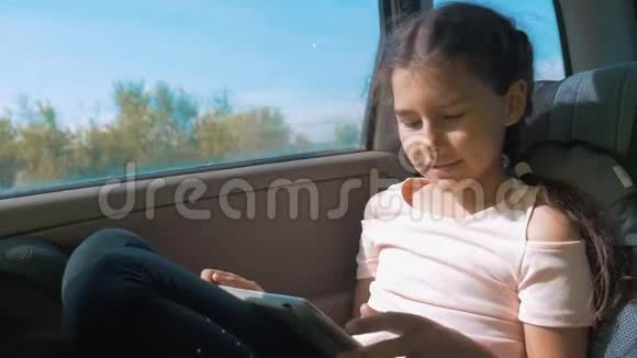 小女孩坐在车里带着平板电脑互联网社交媒体去旅行汽车概念旅行运输运动视频的预览图