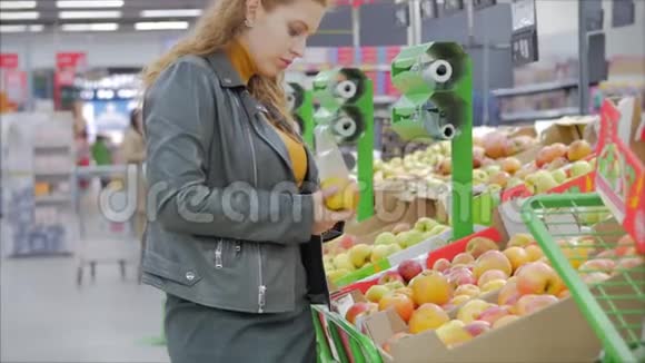 漂亮的年轻漂亮的红发女人在市场上在超市里买食物水果苹果女孩选择视频的预览图