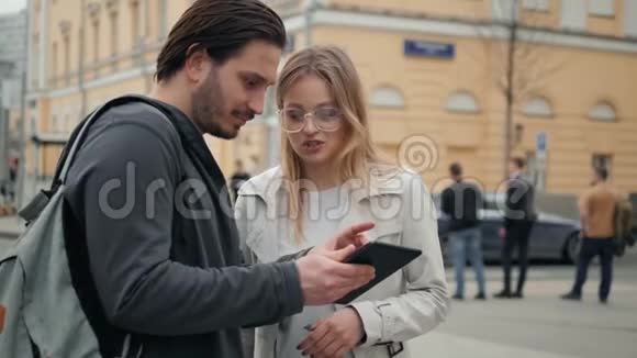 在户外使用平板电脑的情侣男人和女人使用电话电脑导航年轻的学生游客视频的预览图
