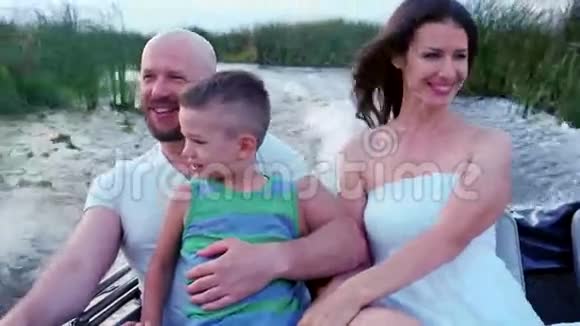 快乐的母亲父亲和儿子伸出双手享受假期幸福的家庭坐在船上父母带着孩子视频的预览图