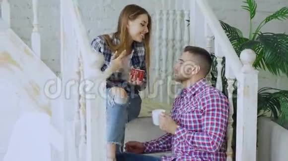 年轻快乐可爱的一对夫妇在家中坐在楼梯上喝茶聊天视频的预览图