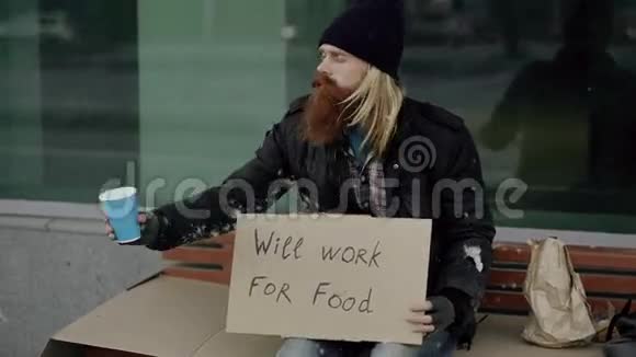 无家可归的年轻人乞求金钱摇晃杯子注意人们在城市人行道上走在乞丐附近视频的预览图