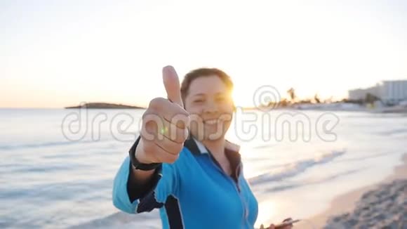 微笑女性健身节目在海滩上竖起大拇指视频的预览图