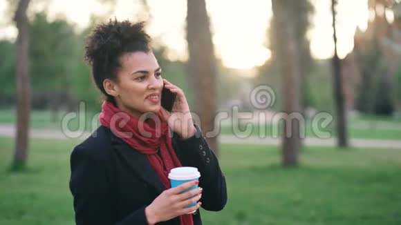 迷人的混合种族女孩交谈智能手机和喝咖啡在城市公园与包年轻女子购物后视频的预览图