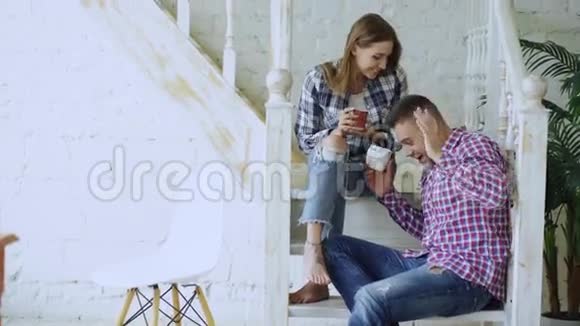 年轻快乐可爱的一对夫妇在家中坐在楼梯上喝茶聊天视频的预览图