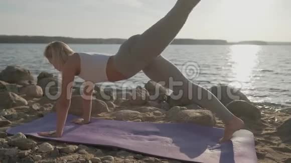 那个美丽的运动女子在海滨做早操海滩和日出的背景视频的预览图