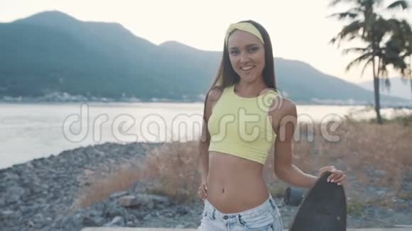 美丽的微笑的年轻女子在海边摆着长板视频的预览图