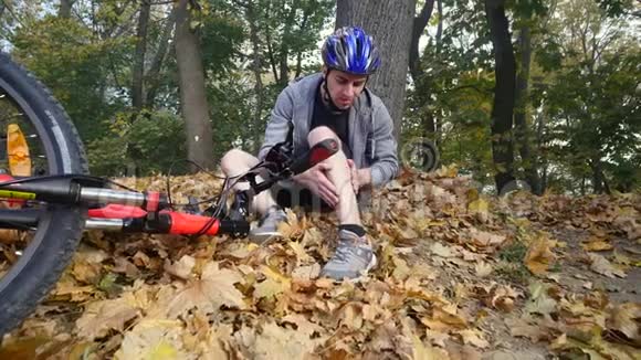 一个年轻人从一辆自行车上摔下来后坐在公园里缓解膝盖的疼痛在公园里骑一辆危险的自行车视频的预览图