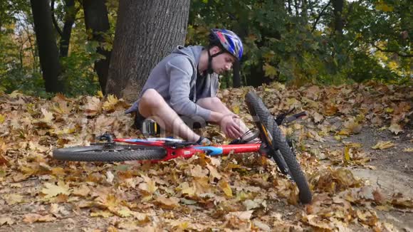 一个年轻人从一辆自行车上摔下来后坐在公园里缓解膝盖的疼痛在公园里骑一辆危险的自行车视频的预览图