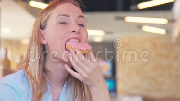 靠近一个正在吃面包圈的女人带着五颜六色的糖霜和微笑视频的预览图