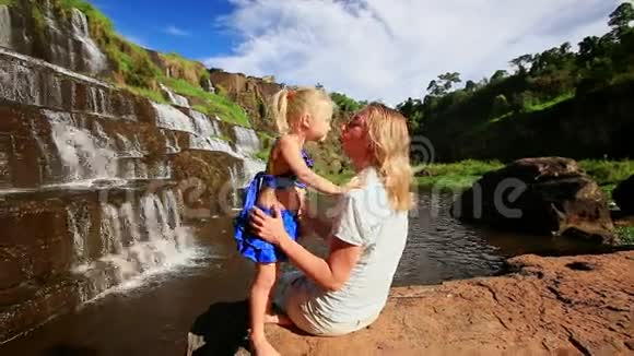 妈妈和小女孩一起坐在石头上一起坐在瀑布旁视频的预览图