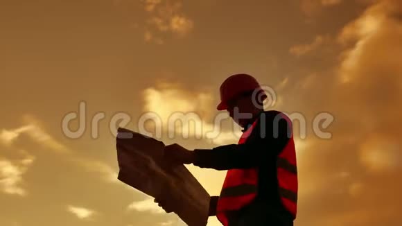工人剪影工人建设者男子与红色头盔和牛仔裤衬衫附近的工业墙剪影工人生活方式视频的预览图