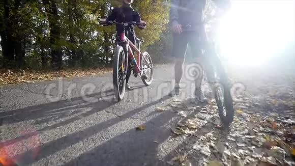 漂亮的夫妇在秋天的公园里骑自行车散步阳光背景慢动作视频的预览图