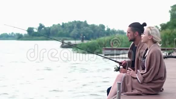 男孩和女孩在码头上聊天男人在湖边钓鱼在湖边寒冷的早晨视频的预览图