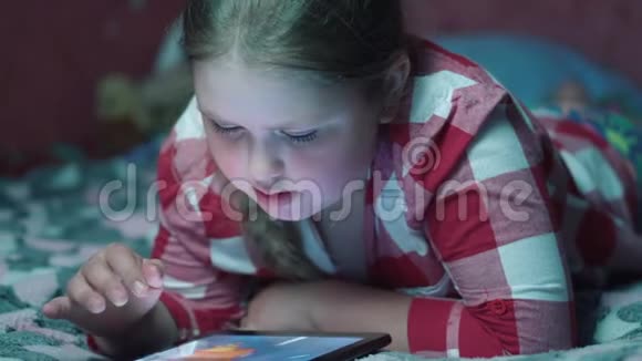 金发女孩在平板电脑上玩游戏晚上躺在沙发上4k视频的预览图