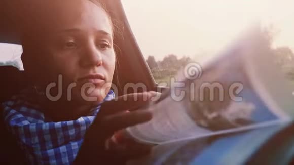 美丽的黑发女人在美丽的夕阳下在汽车里旅行时看书3840x2160视频的预览图
