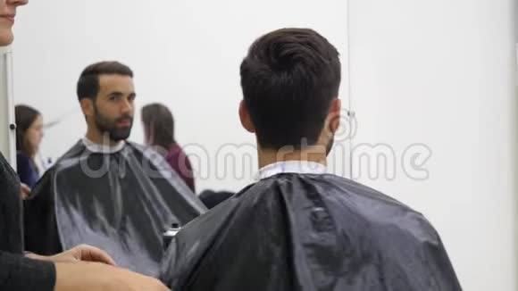 专业的理发师用镜子向英俊而满意的男性客户展示理发的背面视频的预览图
