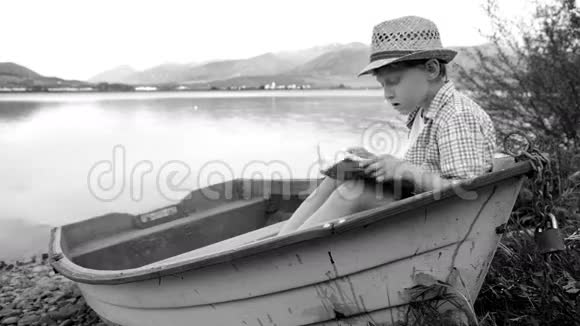 一个男孩坐在湖边的小船上读着黑白照片视频的预览图