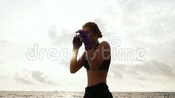 运动的年轻女子在海上背着太阳打拳击美丽的女拳击手在海滩上训练视频的预览图
