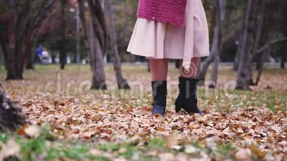 穿着米色连衣裙的女人在秋天的公园里扔树叶在慢动作中玩得很开心她的腿3840x21604k视频的预览图
