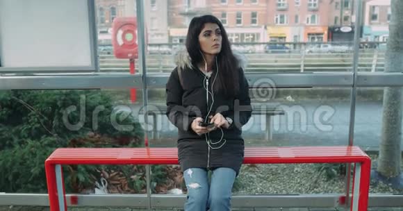 年轻女子环顾四周在公共汽车站等公共汽车红回声4k视频的预览图